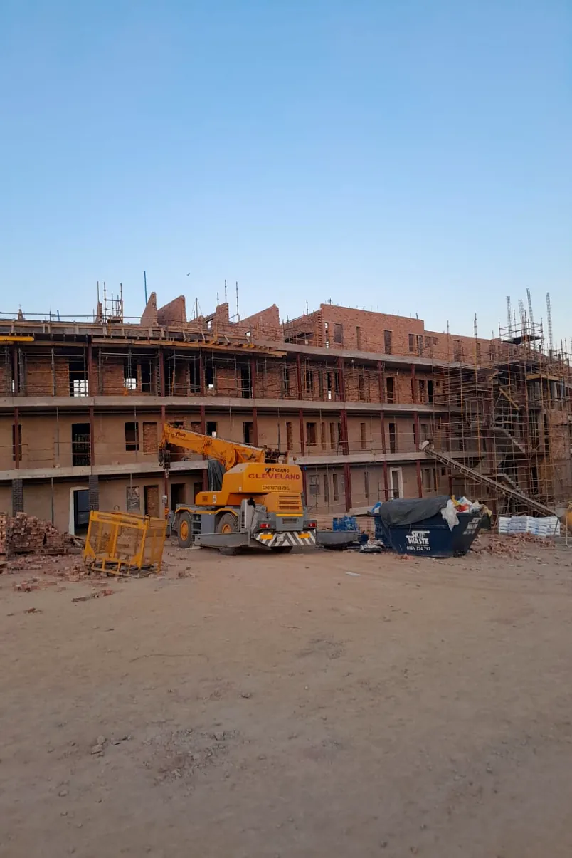 Multi-storey brick building under construction with a mobile crane on site